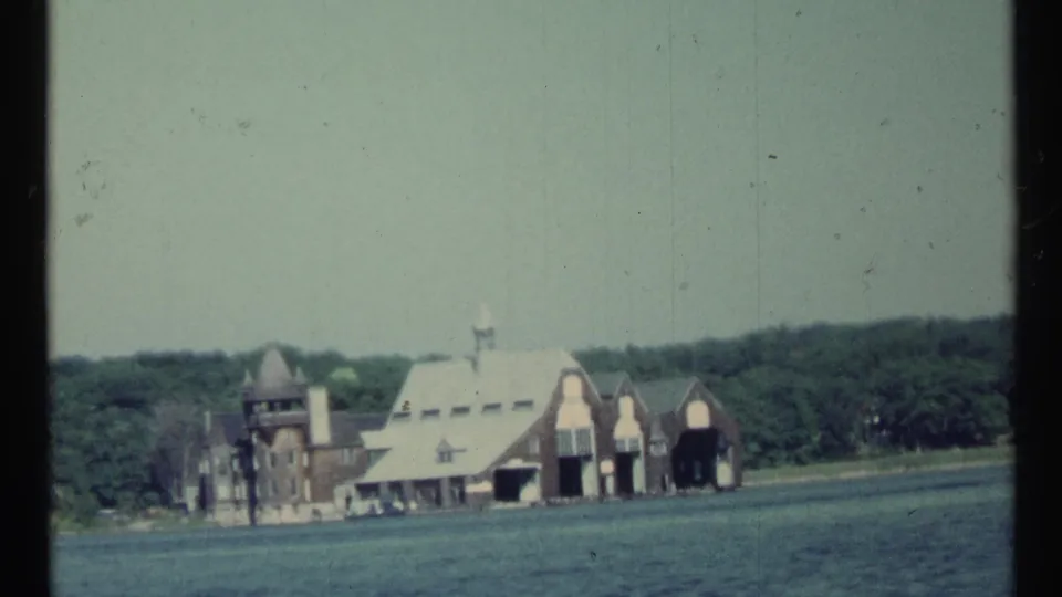 1967 8mm view of an estate-like lakeside complex with a tower, steep roofs, and broad openings along the water.