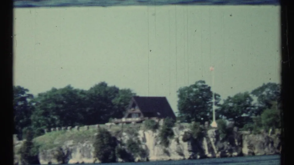 Soft 8mm frame of the lakeside A-frame cabin and rocky bank, with motion blur from the boat.