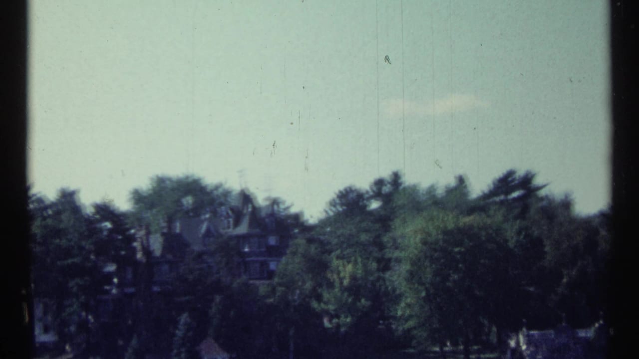 Distant Toronto riverfront view on 8mm film, with a mansion-like building emerging above trees.