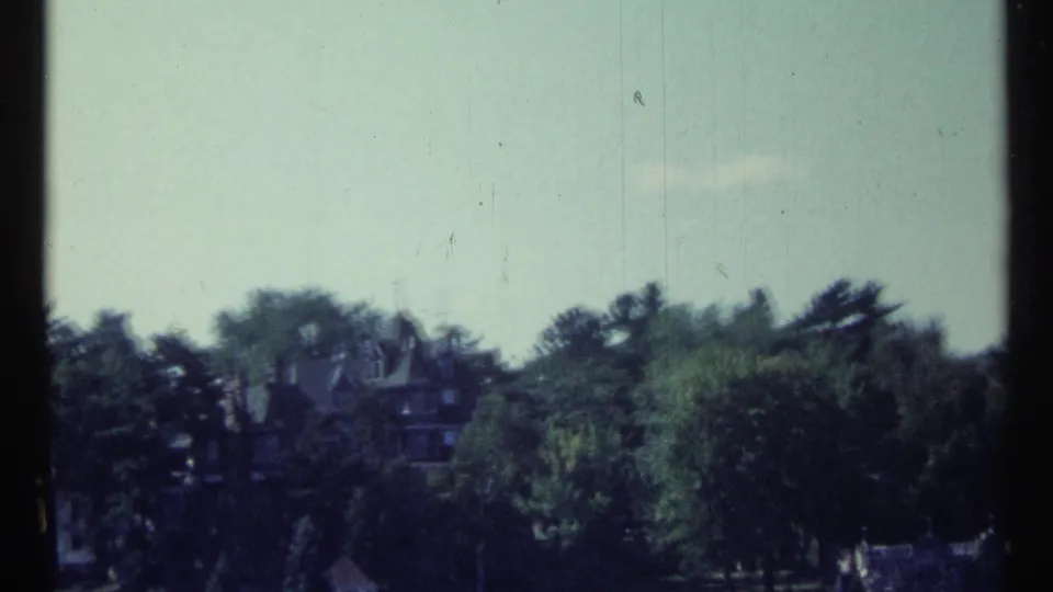 Distant Toronto riverfront view on 8mm film, with a mansion-like building emerging above trees.