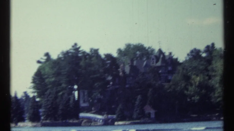Softly focused 1967 Toronto 8mm frame showing water, a wooded bank, and a distant castle-like mansion.
