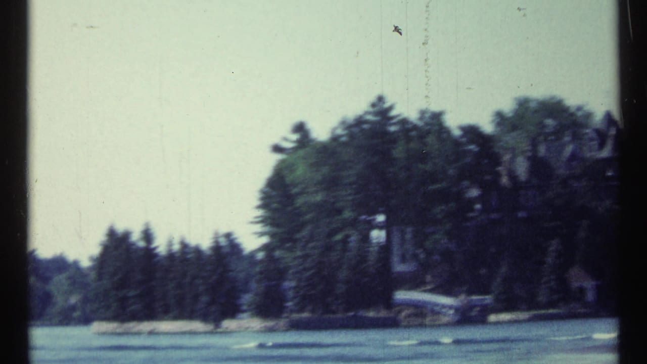 1967 8mm view near Toronto showing lake water, trees, and a partly visible castle-like estate beyond the shoreline.