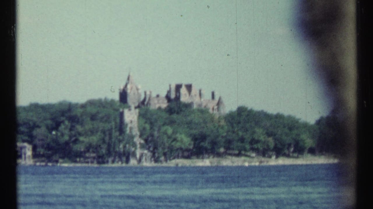 Castle-like estate rising above trees on an island across calm water.