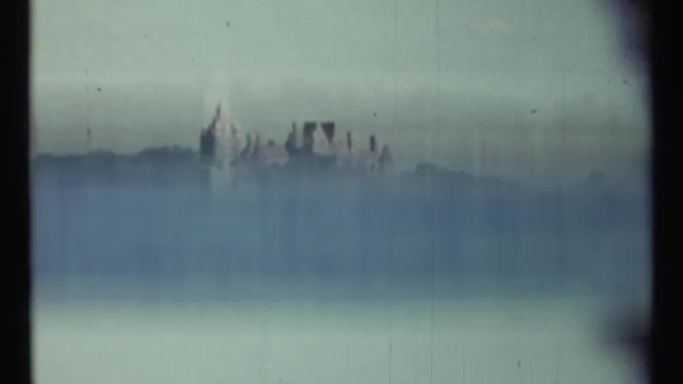 Soft, hazy 1967 8mm frame of the castle-like estate across the lake, partly obscured by exposure and film texture.