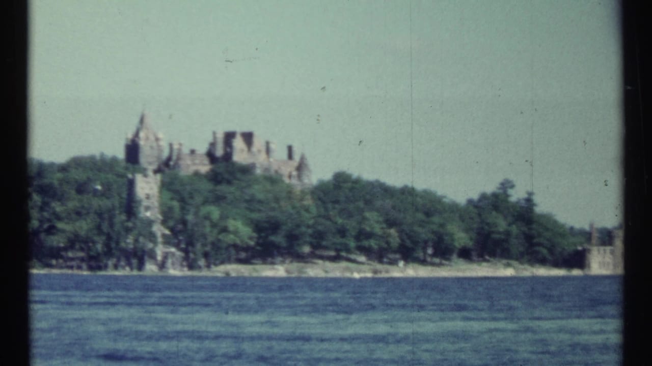 1967 Toronto home-movie view of a castle-like lakeside estate seen across water, with turrets rising above trees.