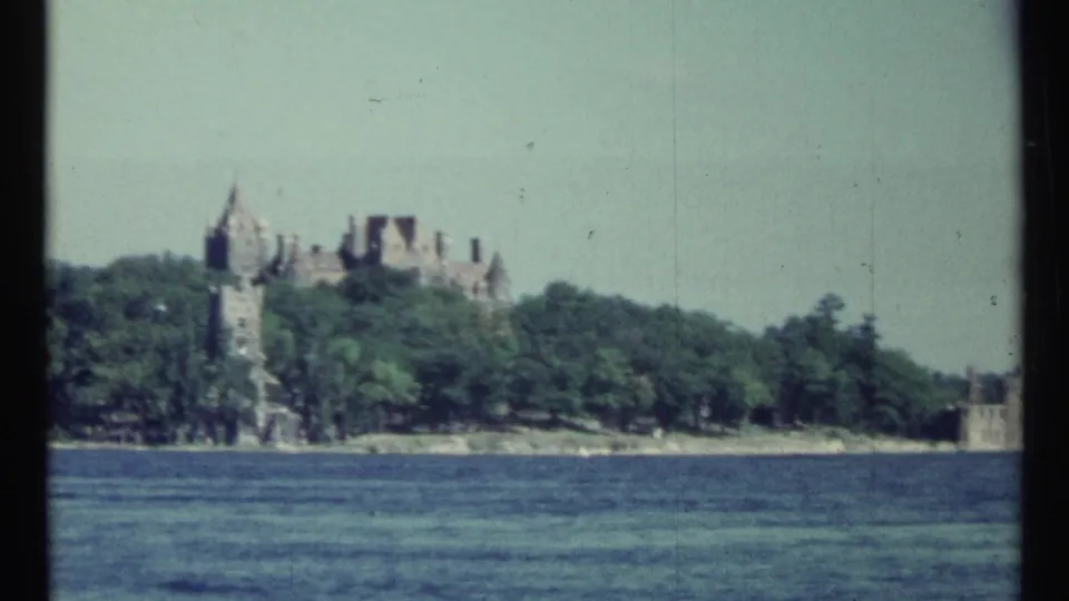 1967 Toronto home-movie view of a castle-like lakeside estate seen across water, with turrets rising above trees.