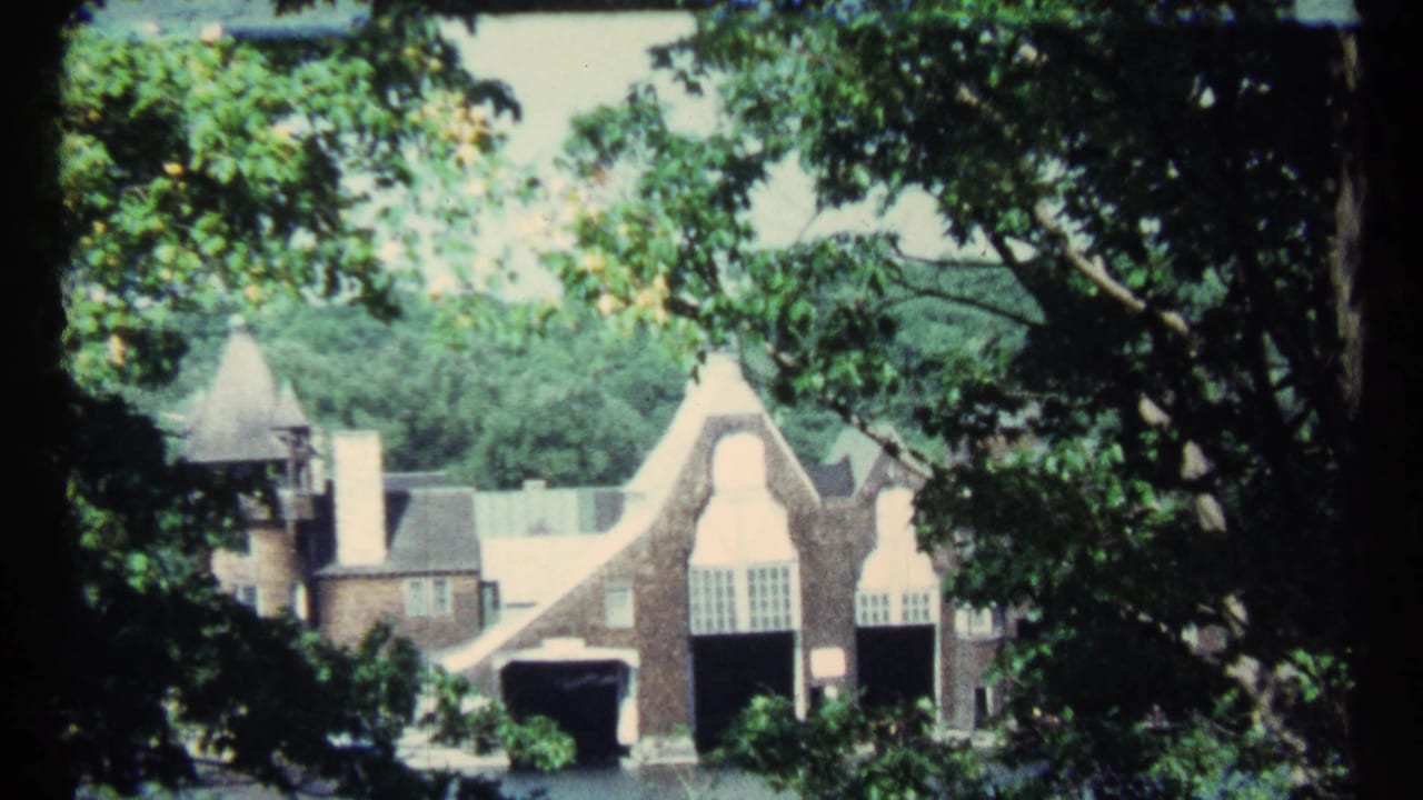 Gabled brick house and tower viewed through dark tree branches and bright green foliage.