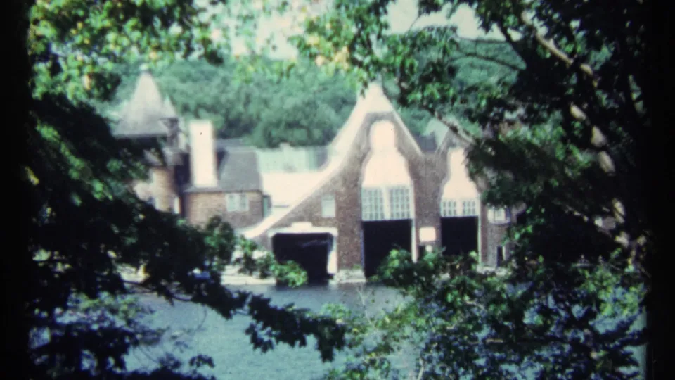 1967 Toronto 8mm frame of a large gabled brick house beyond water, partly covered by surrounding green trees.