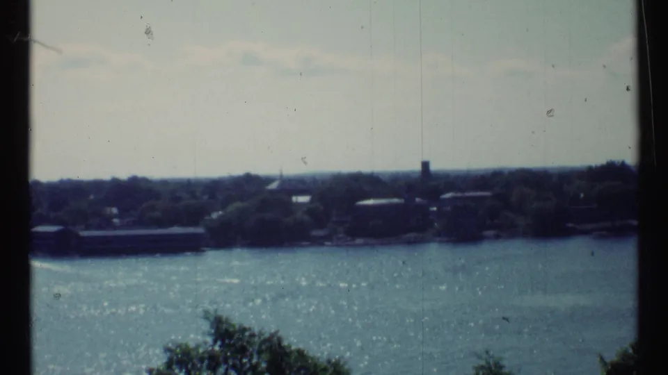1967 8mm view across a Toronto-area river toward trees, low buildings, and a bright water surface.