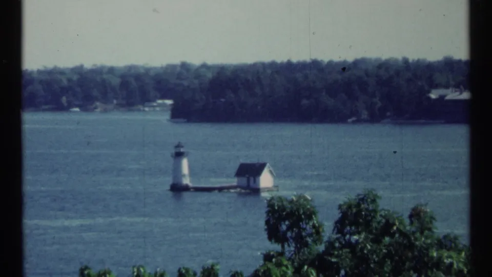 1967 Toronto waterfront frame showing a small white lighthouse-like structure beside a small house on a platform in the river.