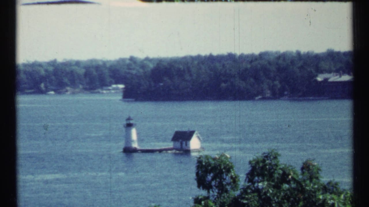 Lighthouse and small white lakeside building with trees in the foreground.