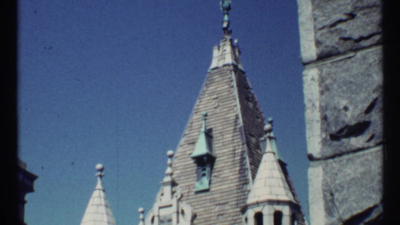Gothic-style roof spires beside a rough stone wall under blue sky.