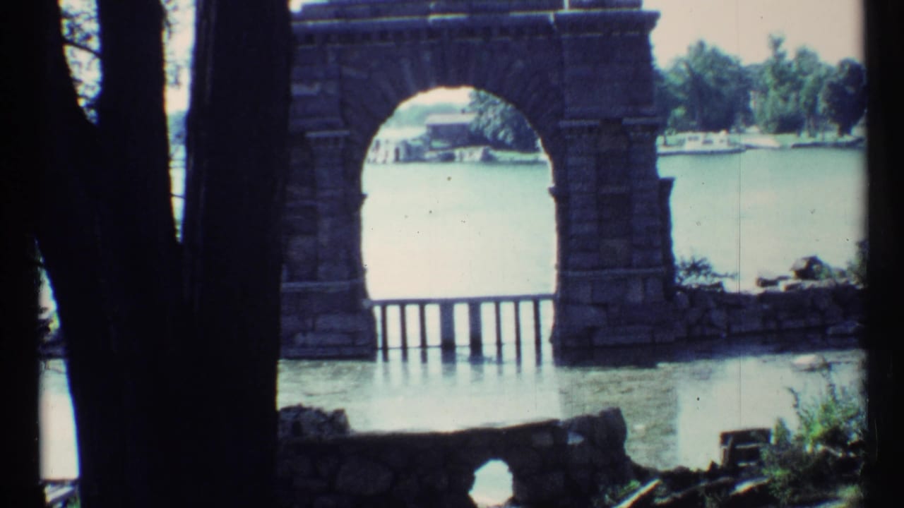 Stone archway frames a lake with trees and small boats beyond.
