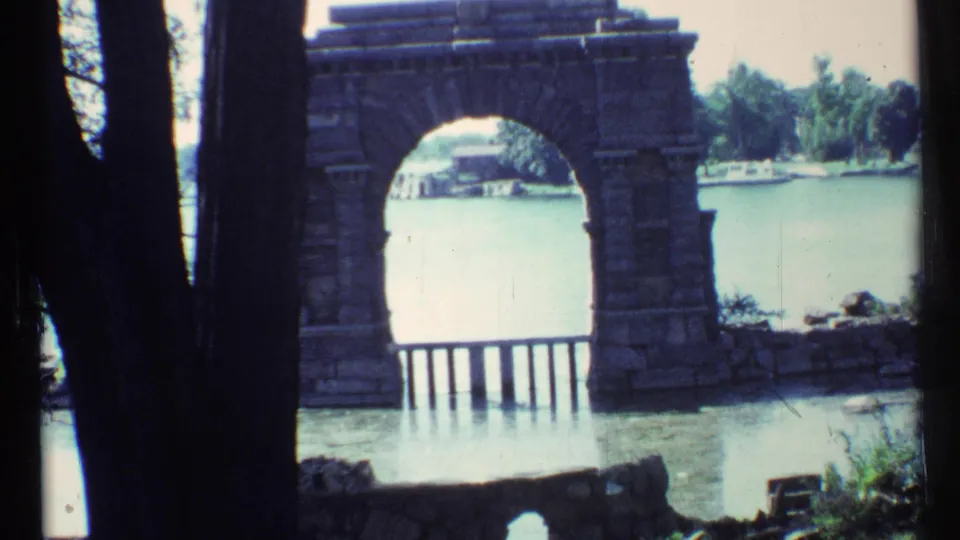 Visitor-shot 1967 Toronto view of a stone arch near the lake, with railing posts, trees, and distant shoreline through the opening.