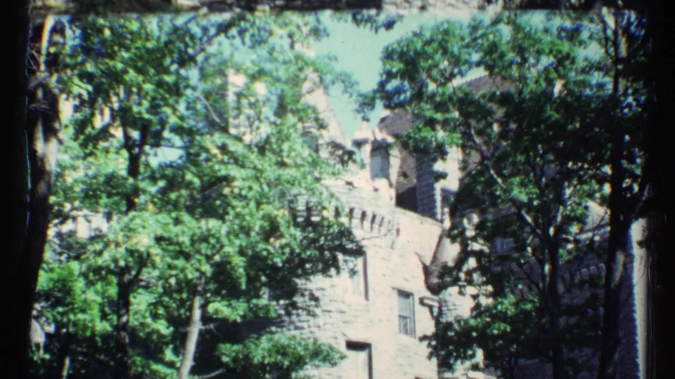 A 1967 Toronto home-movie view of green trees in front of a stone building with battlement-like architectural details.