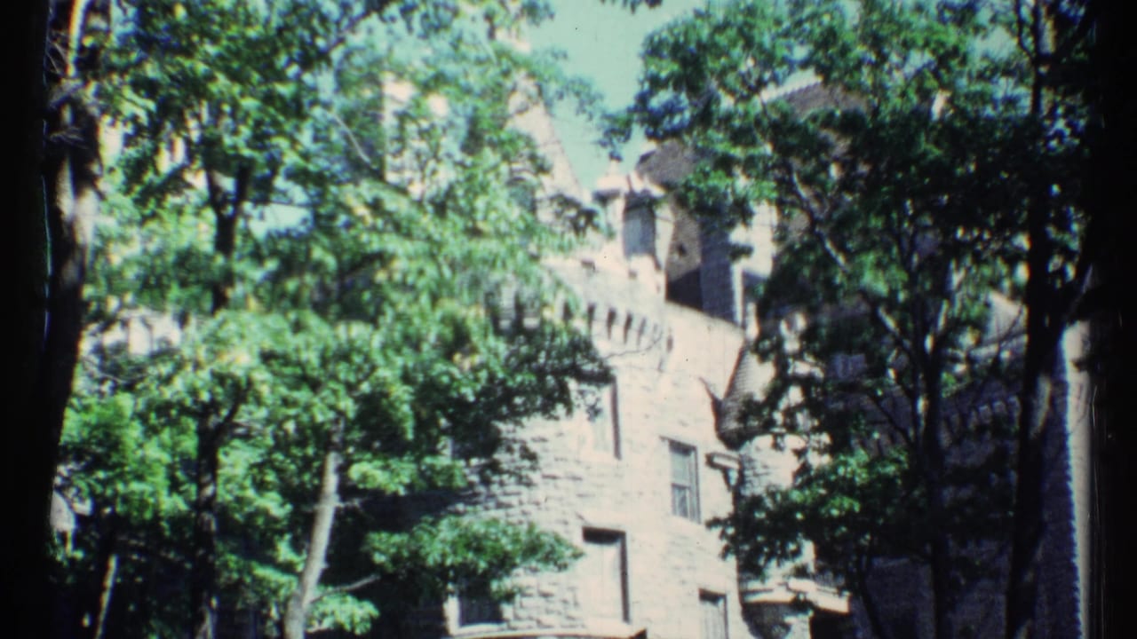 1967 Toronto home-movie frame showing a crenellated masonry building behind dense green trees.