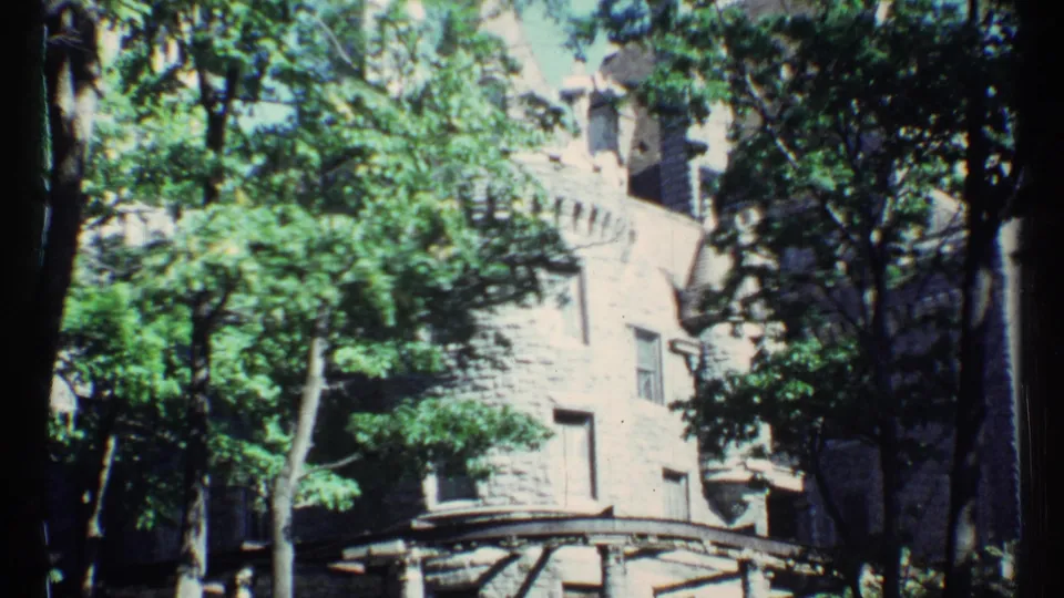 1967 Toronto frame with a stone-like building facade obscured by tall trees and foliage.