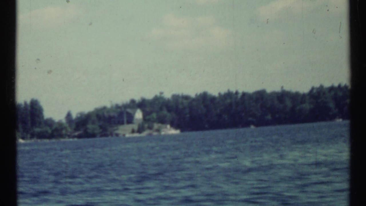 Rippling blue water with a distant wooded shoreline and small pale structure.