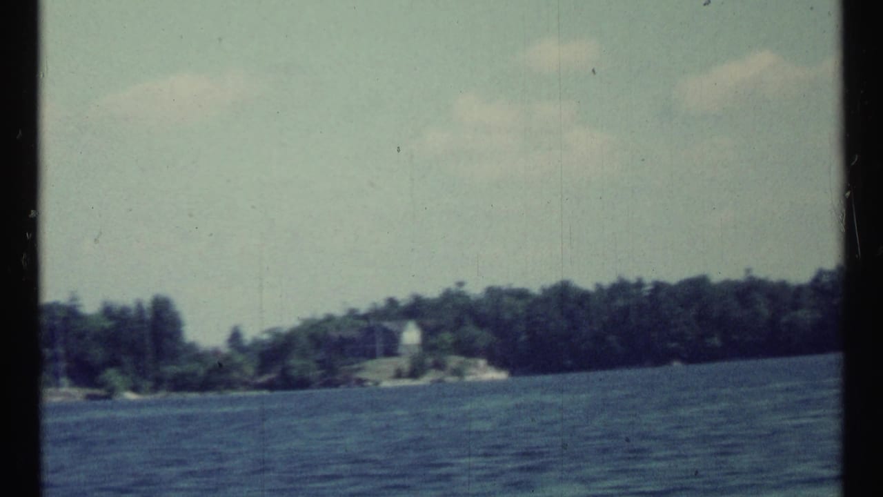 Wide lake view with dark blue water, trees, and a small white shoreline structure.