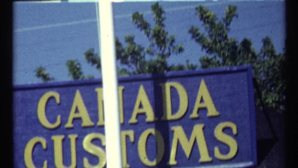 Clearer 1967 Toronto frame of a blue Canada Customs sign with yellow lettering, trees, sky, and a white foreground bar.