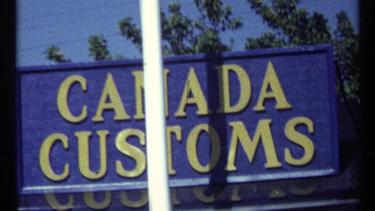 Blue Canada Customs sign with yellow lettering partly blocked by a white pole.