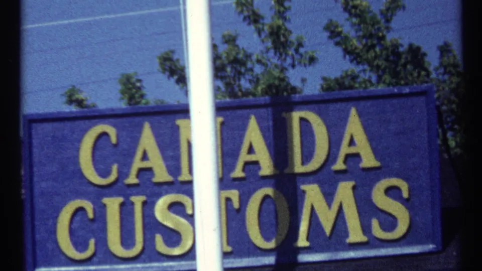 Canada Customs sign in a 1967 Toronto-area travel frame, with a vertical white pole obscuring part of the yellow lettering.