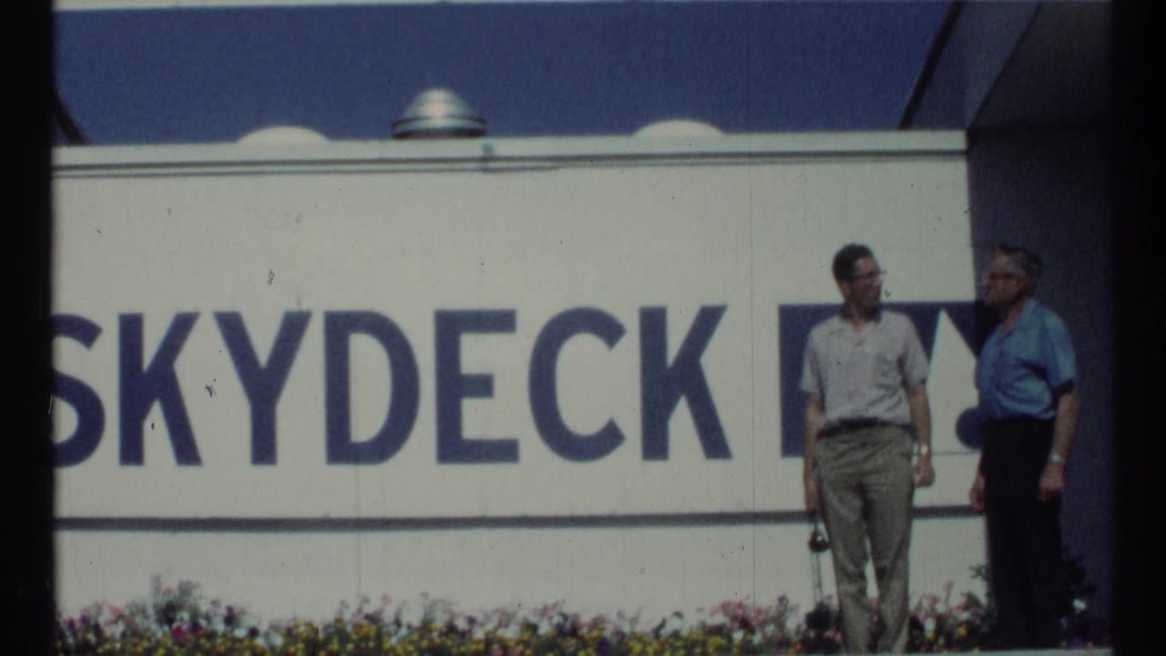 Two men face each other near the Skydeck sign, partly framed by dark edges.