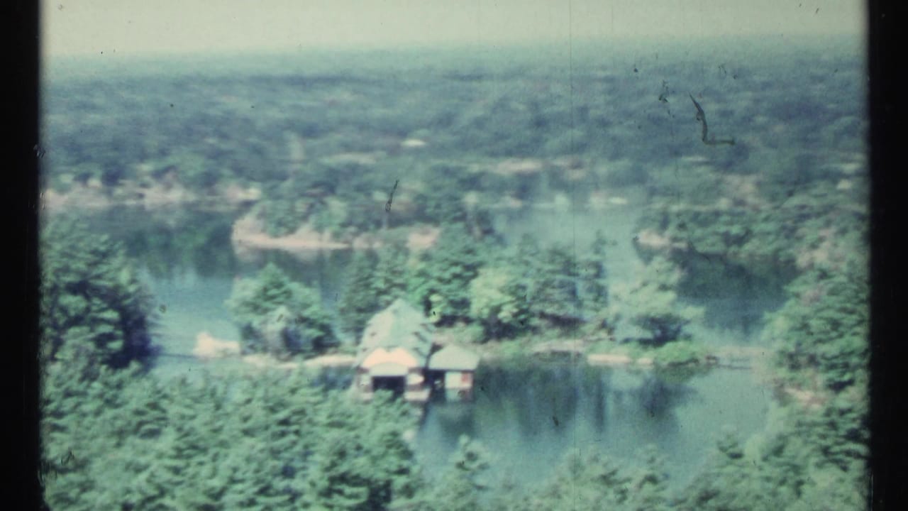 Aerial view of forested shoreline, water channels, and small lakeside buildings.