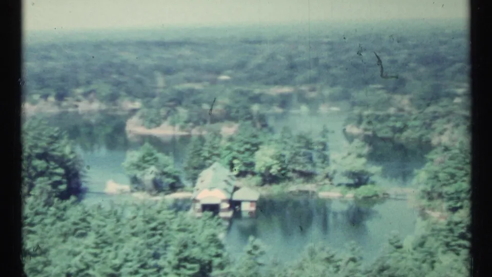 1967 Toronto-area aerial frame with forested shoreline, connected water channels, and small buildings near the water.