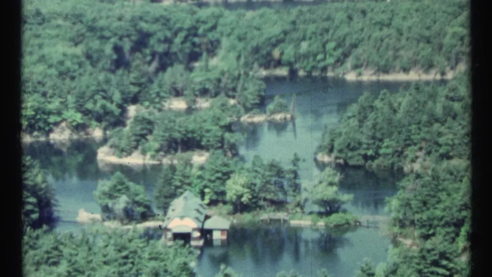 1967 Toronto-area aerial home-movie view of narrow waterways, wooded peninsulas, small docks, and shoreline structures.