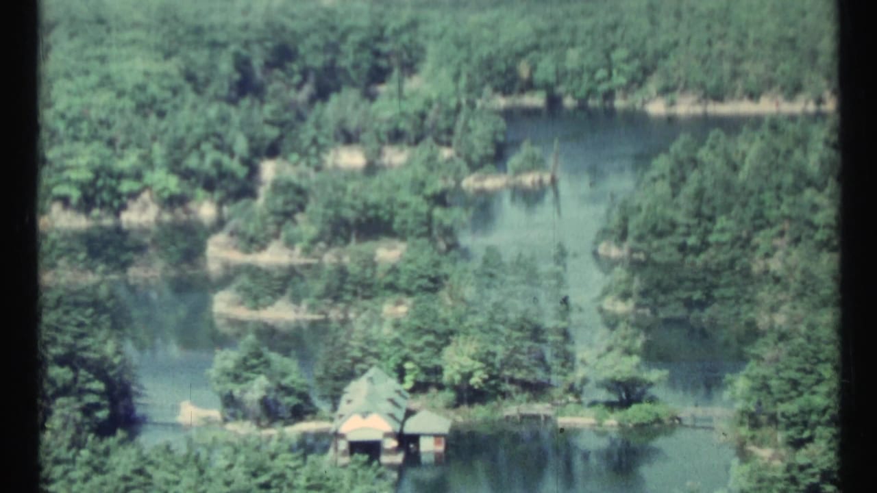 Forested waterway with small islands and a lakeside structure seen from above.