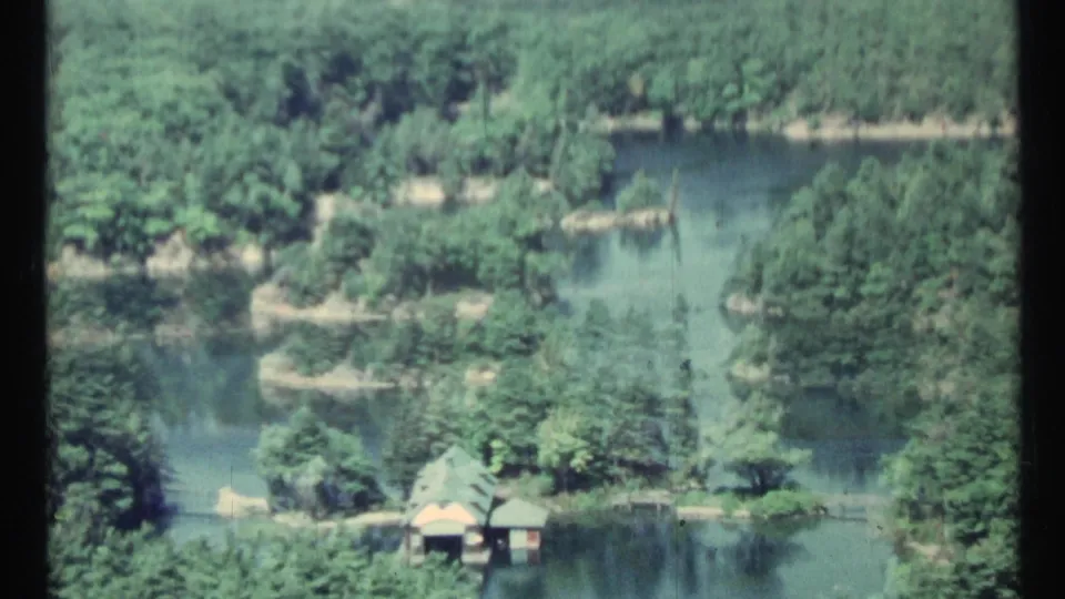 1967 Toronto-area 8mm view of green water, dense trees, small islands, and a small lakeside structure.