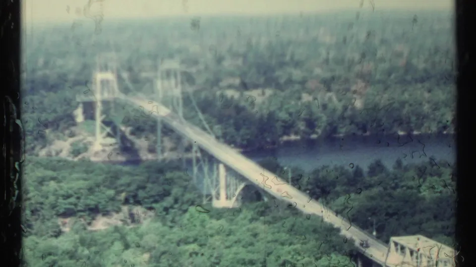 Faded 8mm view of a suspension bridge and river in a densely wooded Toronto-area landscape.