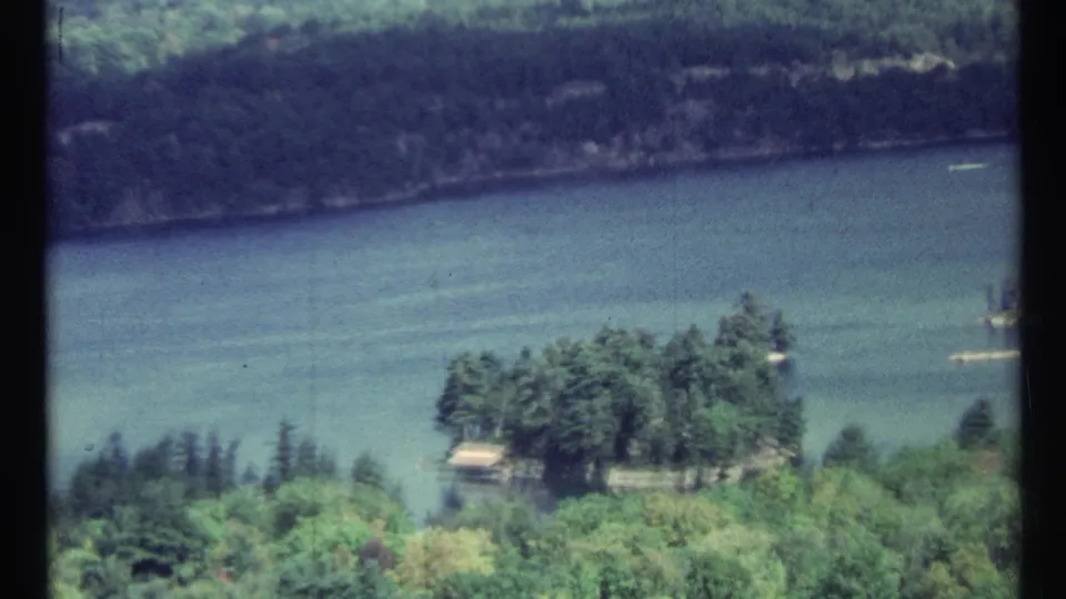 A later frame shows the river and green shoreline from above, with small riverside features and faded 8mm color.
