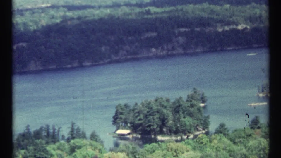 Vintage 1967 8mm view near Toronto with a broad river, distant wooded bank, foreground greenery, and a small island at lower right.