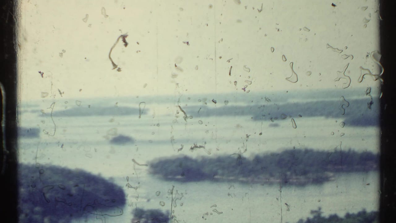 Distant lake with forested islands seen through scratched 8mm film frame.