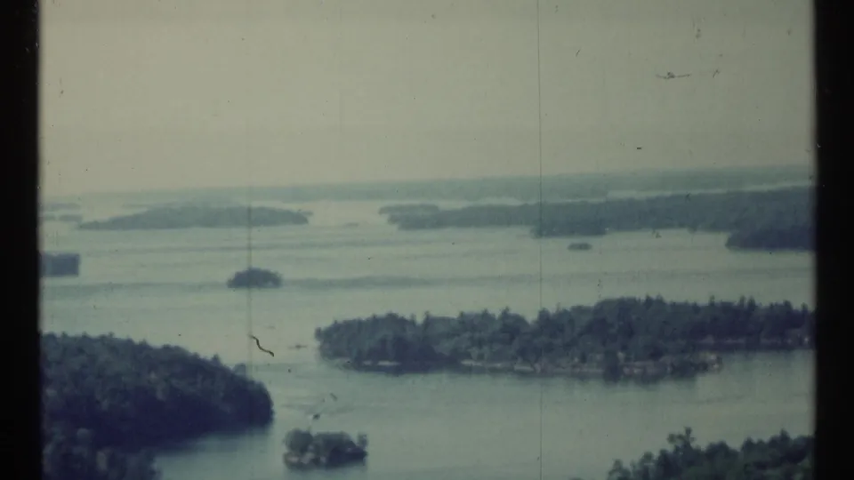 1967 Toronto, Canada home-movie frame showing a wide lake, several tree-covered islands, and softened blue-green 8mm color.