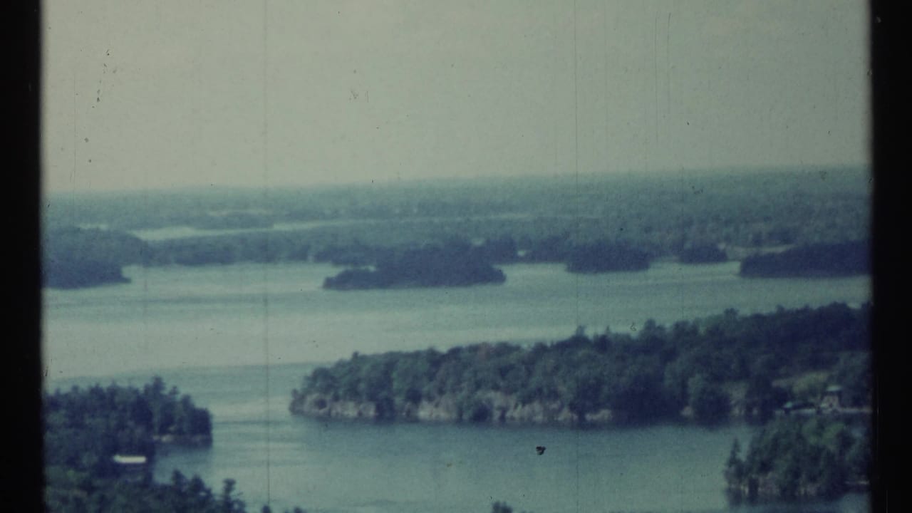 Wide water view with tree-covered islands beneath a pale sky and dark film edge.