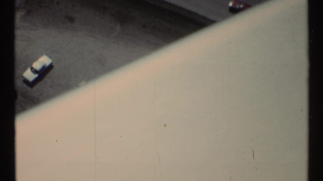 A parked car on asphalt appears beyond a large pale diagonal structure.