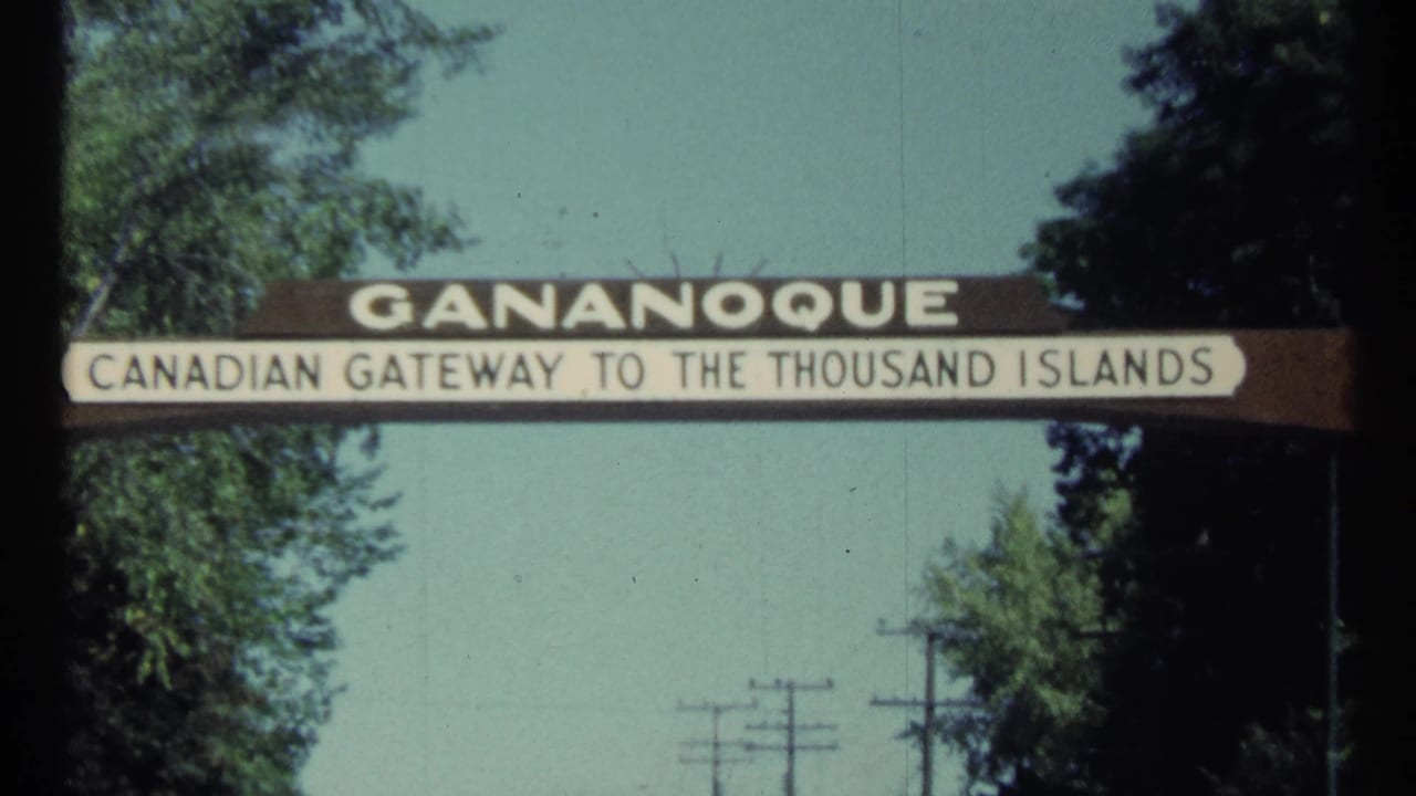 Gananoque gateway sign spanning a road with trees and utility poles behind it.