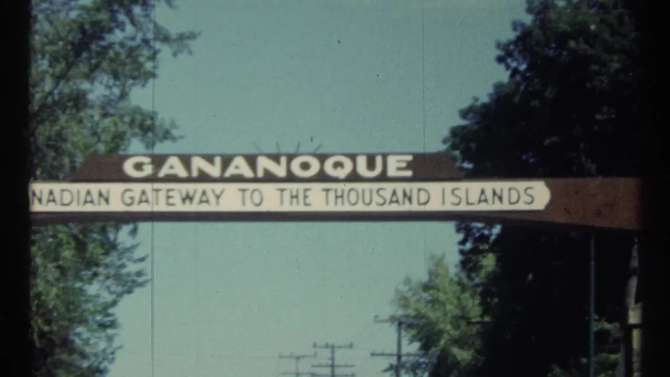 1960s Canadian travel frame centering the Gananoque Canadian Gateway to the Thousand Islands sign beneath blue sky and roadside trees.