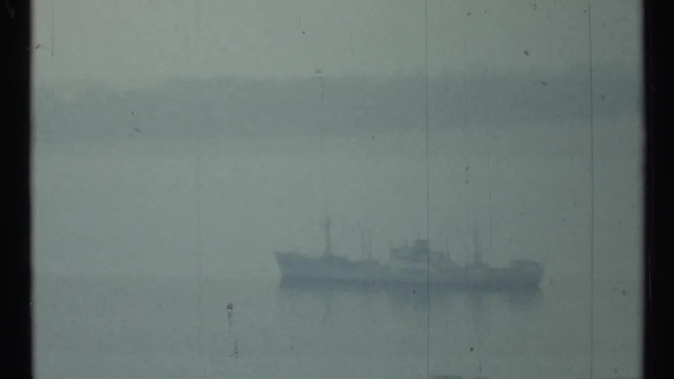 Large distant vessel, possibly naval, sits in haze on Toronto harbor water in a soft 1960s 8mm frame.