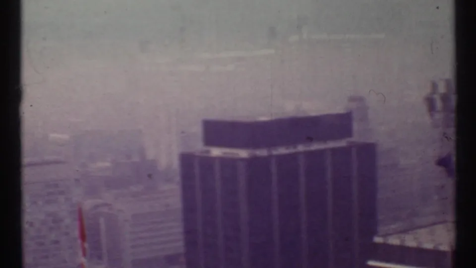 Elevated 1967 Toronto view with a dark rooftop form in the foreground and foggy buildings beyond.
