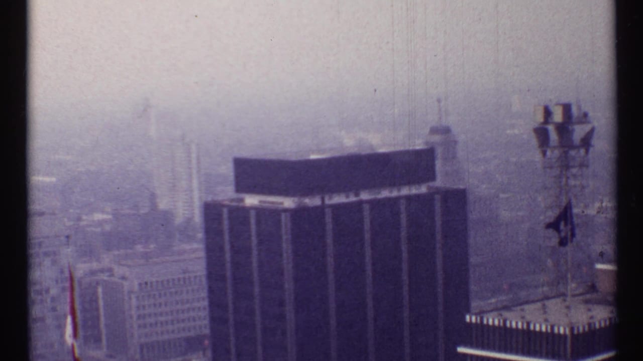 Hazy high-angle view of a dark office tower and nearby rooftop equipment.
