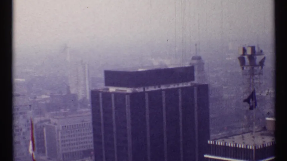 1967 Toronto 8mm frame showing a dark high-rise office building through haze with rooftop equipment at right.