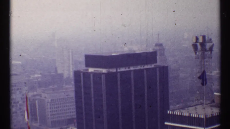 1967 Toronto skyline frame with a dark office tower, rooftop structure, and distant buildings softened by haze.