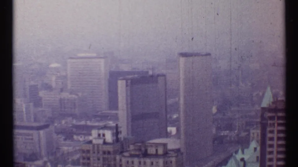 1967 Toronto skyline frame with office towers, low rooftops, and a pale blue roof detail softened by haze.