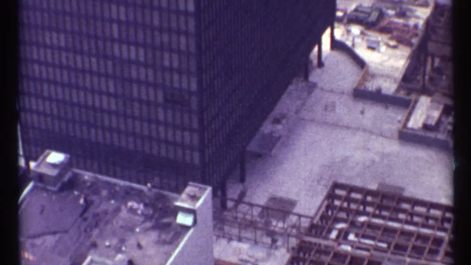 High-angle 1967 Toronto view of modern dark high-rises, a rooftop or work deck, and exposed construction framing near the street.