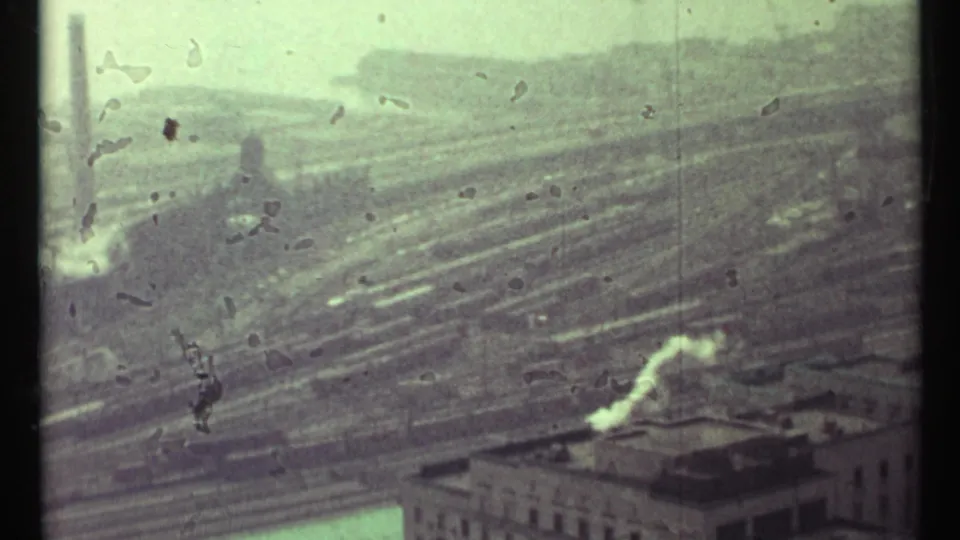 Toronto rail yard seen through aged 8mm film, with dense tracks, rooftop smoke, and scratches across the frame.