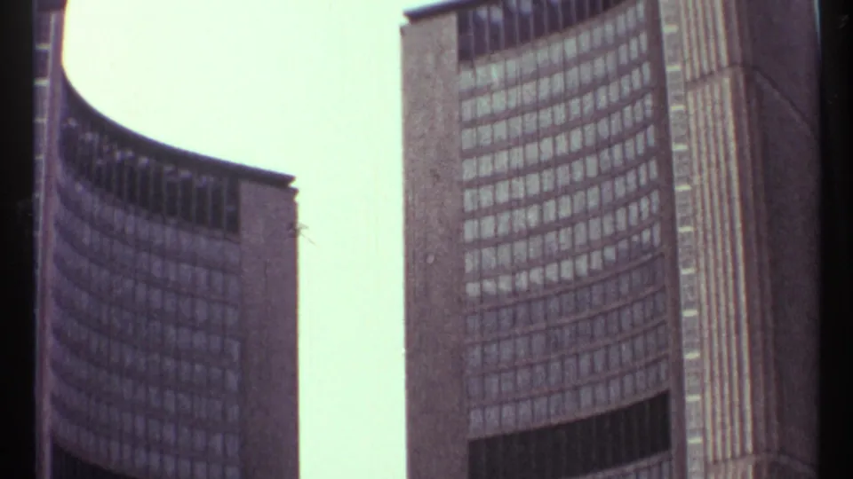1967 Toronto City Hall frame showing the two curved towers rising around a bright vertical gap, with window grids and dark lower openings visible.